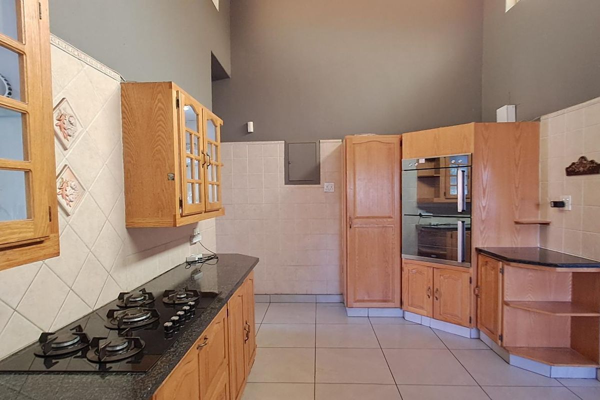 Spacious kitchen featuring wooden cabinetry, built-in oven, gas hob, and tiled flooring with high ceilings.