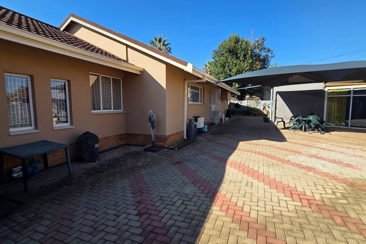 Spacious rear exterior area featuring paved driveway, shade sail covering, and secure window treatments on the building facade.
