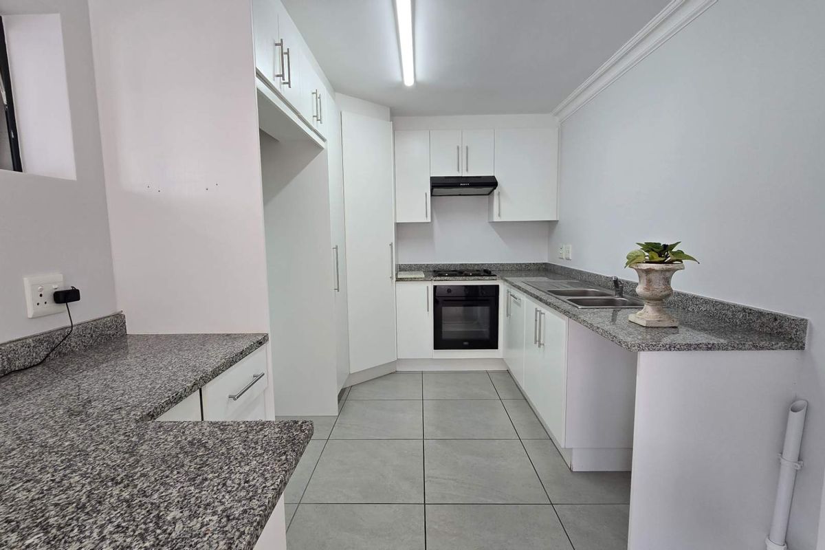 A clean, modern kitchen featuring white cabinetry, granite countertops, a built-in oven, gas hob, extractor fan, and tiled flooring.