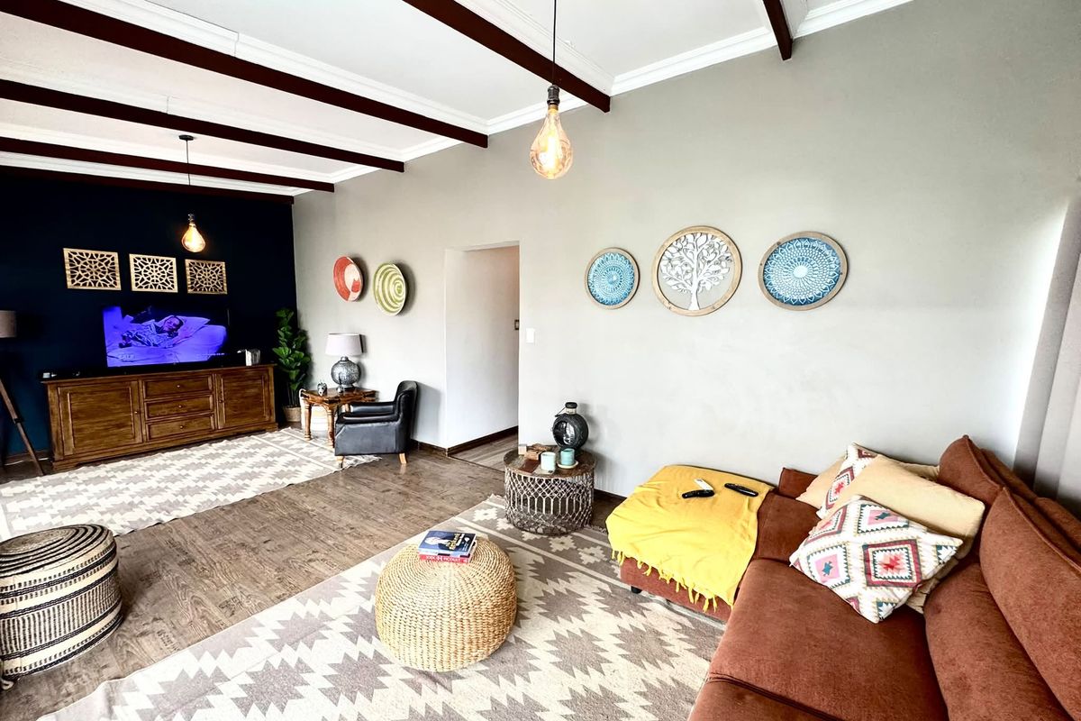 Spacious living room featuring exposed dark timber ceiling beams, laminate flooring, and a feature wall with coved cornicing and modern pendant lighting.