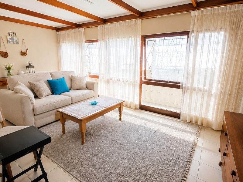 A bright living room featuring exposed timber ceiling beams, tiled flooring, and large windows with access to an outdoor area.