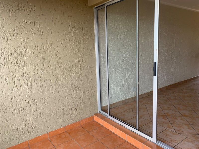 A covered balcony area featuring tiled flooring and a sliding glass door, providing a transition between indoor and outdoor living spaces.