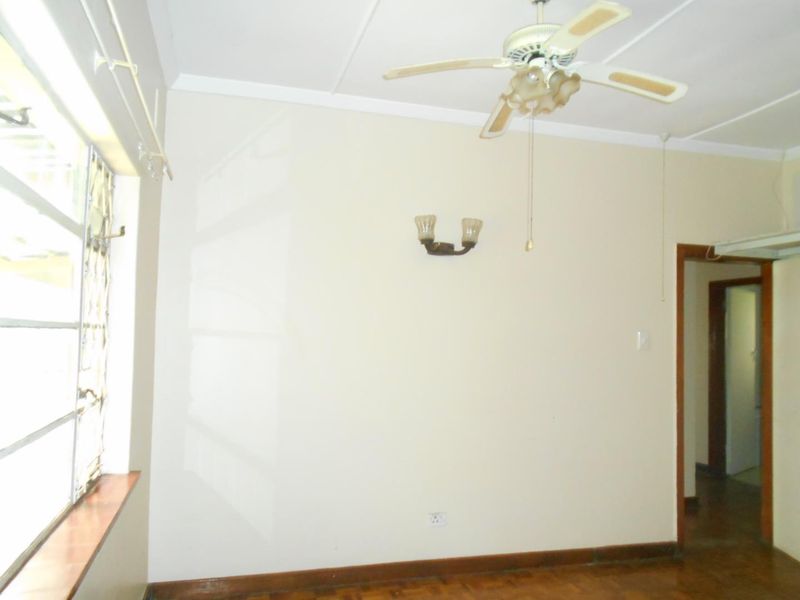 An empty bedroom featuring parquet flooring, a ceiling fan, and wall-mounted lighting, offering a blank canvas for potential interior updates.