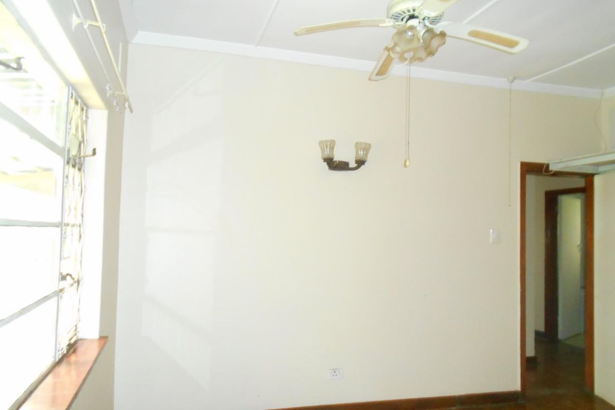 An empty bedroom featuring parquet flooring, a ceiling fan, and wall-mounted lighting, offering a blank canvas for potential interior updates.