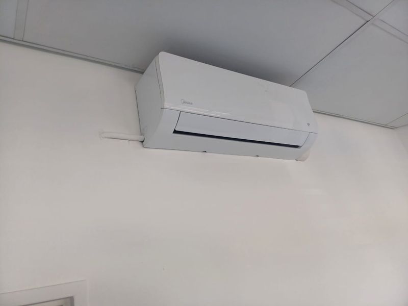 A wall-mounted split-system air conditioning unit installed in an office space with a suspended ceiling.