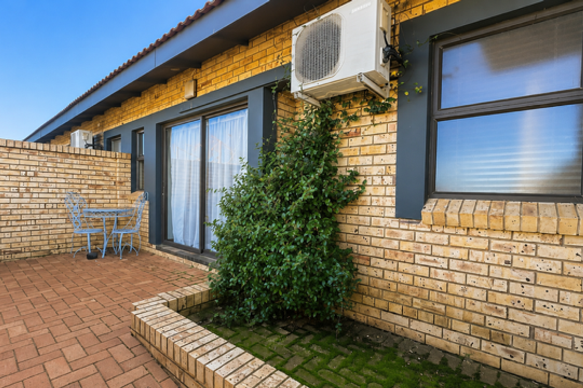 A private rear patio area featuring brick paving, sliding door access, and wall-mounted air conditioning unit.