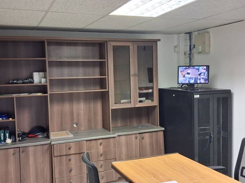 Functional office space featuring extensive built-in wooden cabinetry, a dedicated server rack, and a suspended ceiling with integrated lighting.