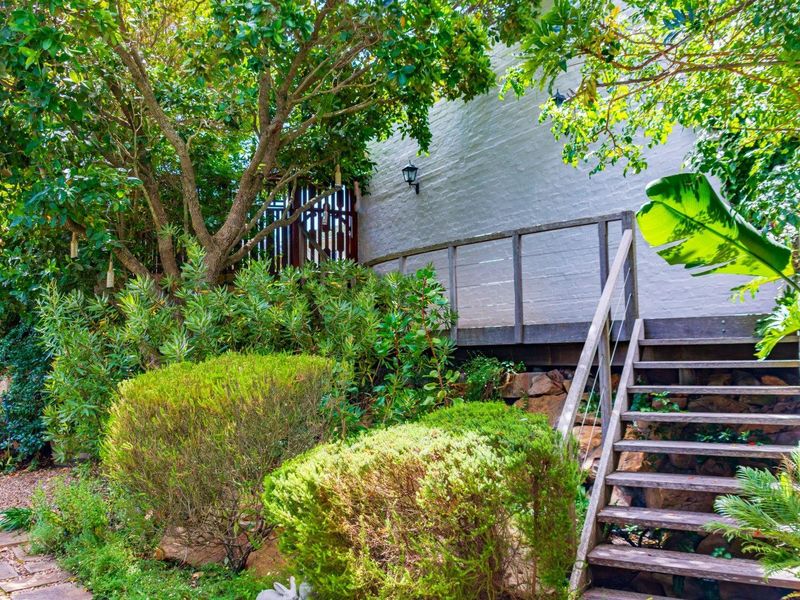 A lush garden area featuring a timber staircase leading to an elevated walkway, complemented by stone retaining walls and mature landscaping.