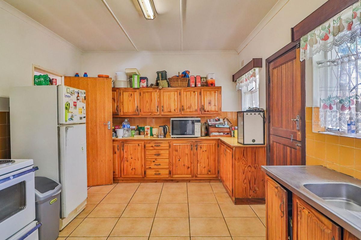 A functional kitchen featuring wooden cabinetry, tiled splashbacks, and tiled flooring, offering a traditional layout with built-in cooking appliances and a stainless steel sink.
