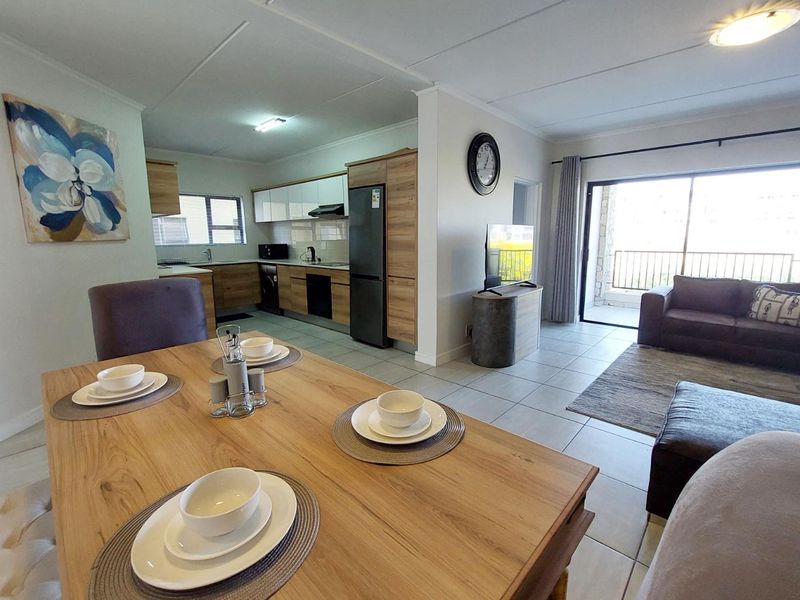 Open-plan living and dining area featuring tiled floors, modern kitchen cabinetry, and direct access to a private balcony through sliding glass doors.
