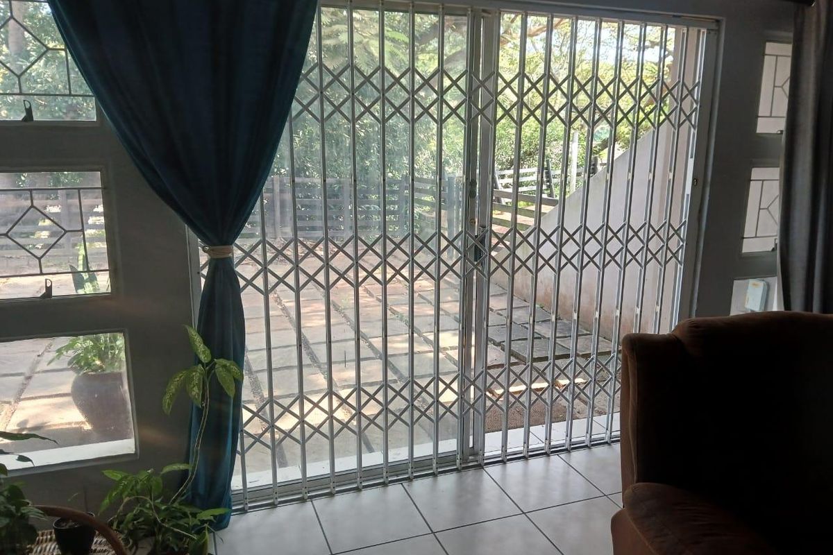 Living area featuring tiled flooring and a large glass sliding door secured with a white metal security gate, providing access to the patio.