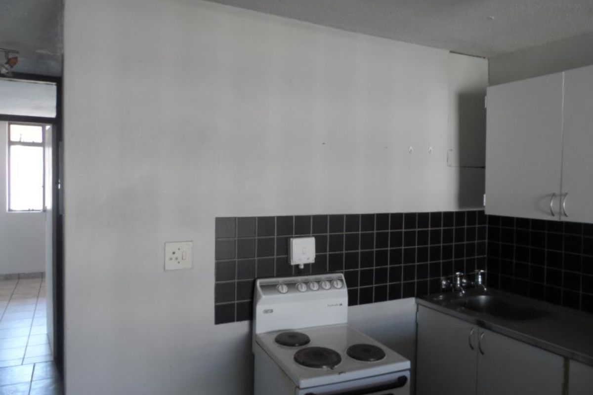 A functional kitchen area featuring a freestanding electric stove, built-in cabinetry, and a stainless steel sink with a black tiled splashback.