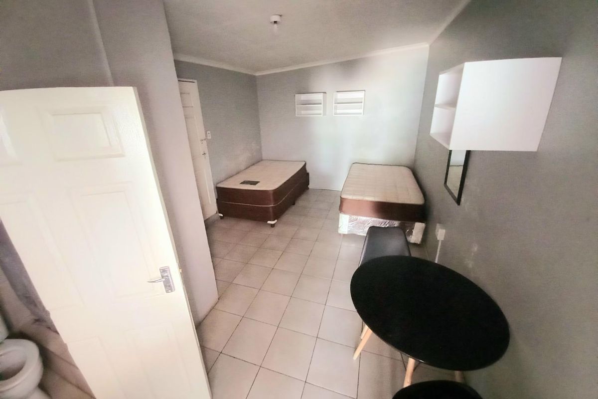 A functional bedroom featuring tiled flooring, built-in wall shelving, and direct access to an en-suite bathroom area.