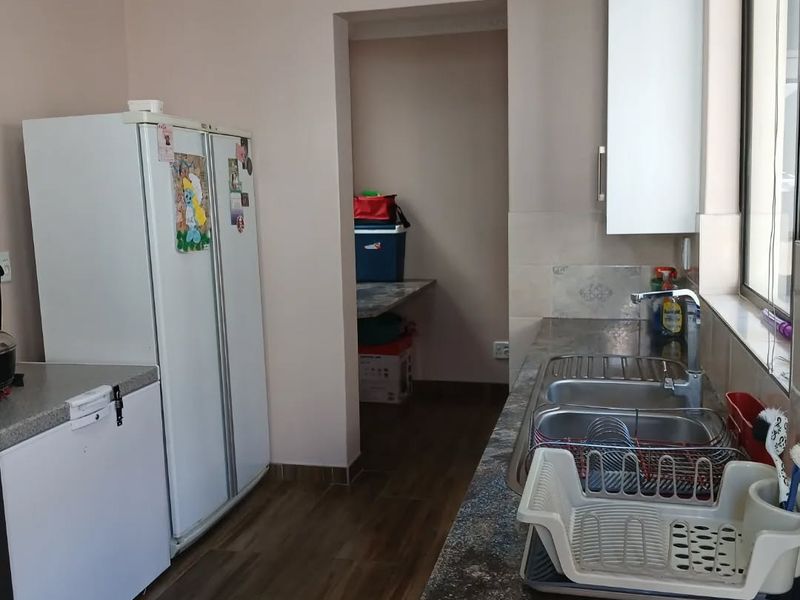 A functional kitchen featuring granite countertops, a double stainless steel sink, and upper cabinetry, with an adjacent scullery or pantry area.