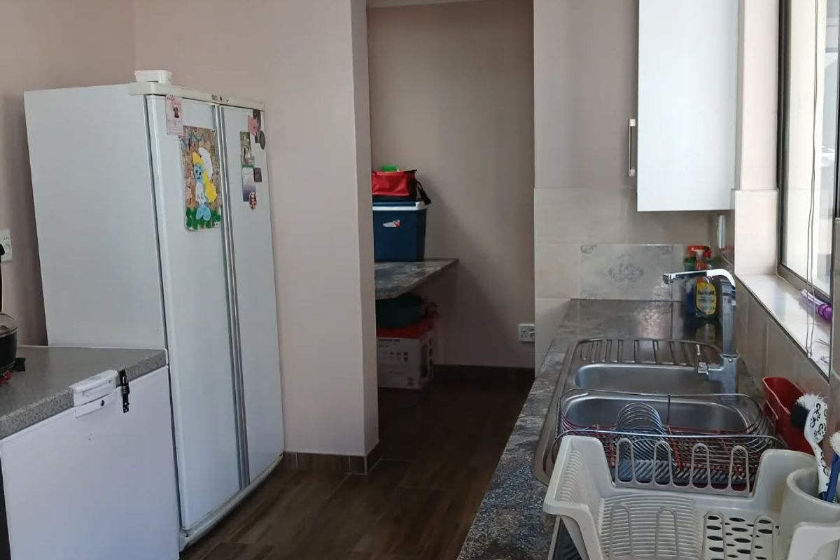 A functional kitchen featuring granite countertops, a double stainless steel sink, and upper cabinetry, with an adjacent scullery or pantry area.
