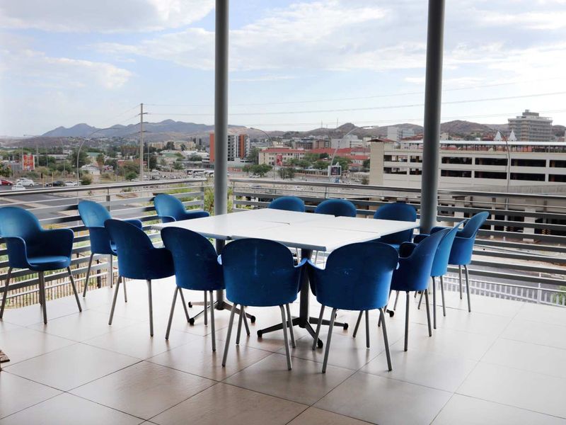 A spacious covered balcony featuring tiled flooring, metal balustrades, and support columns, offering an elevated view of the surrounding urban landscape.