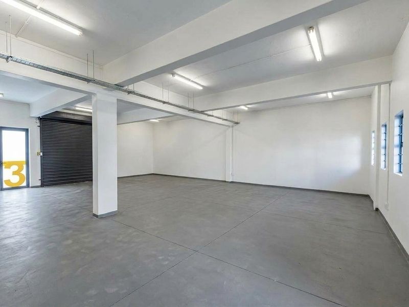 Spacious industrial utility area featuring polished concrete flooring, exposed structural beams, roller shutter door access, and bright overhead fluorescent lighting.
