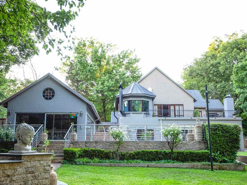 Rear view of the property featuring a multi-level facade, raised patio with metal railings, stone retaining walls, and a well-maintained garden.