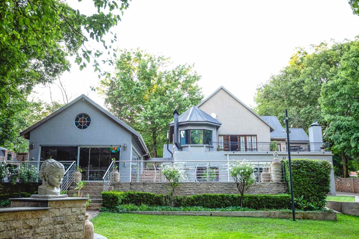Rear view of the property featuring a multi-level facade, raised patio with metal railings, stone retaining walls, and a well-maintained garden.