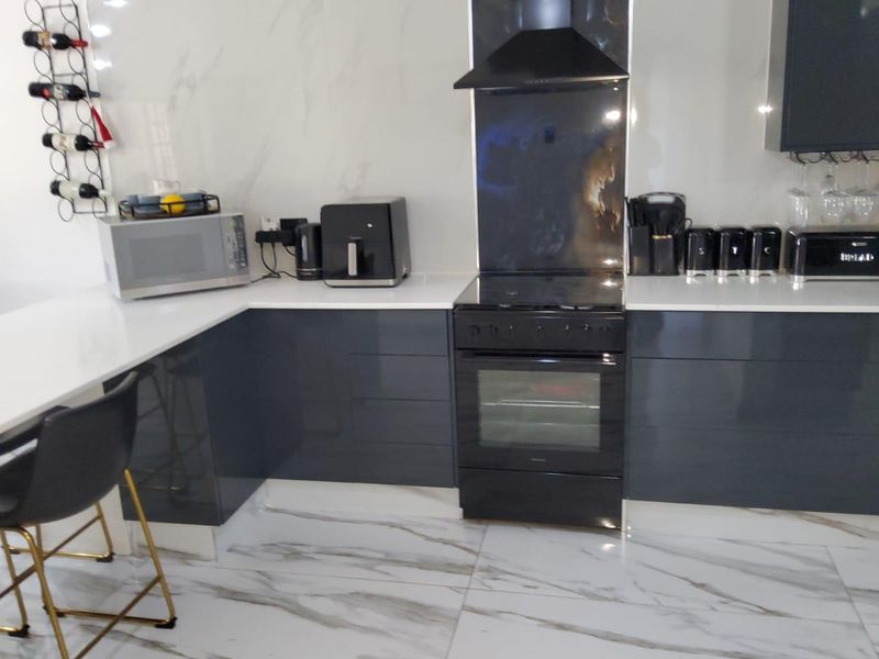 Modern kitchen featuring high-gloss grey cabinetry, white quartz countertops, marble-effect flooring, and integrated black appliances.