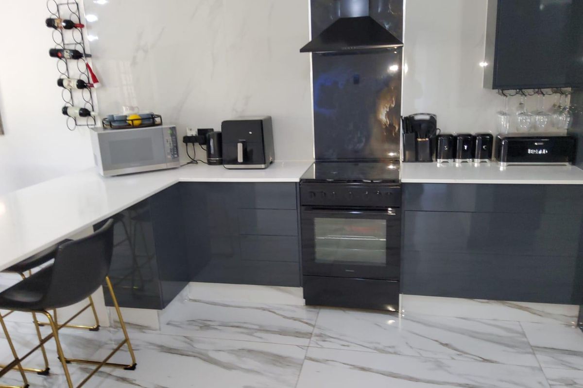 Modern kitchen featuring high-gloss grey cabinetry, white quartz countertops, marble-effect flooring, and integrated black appliances.