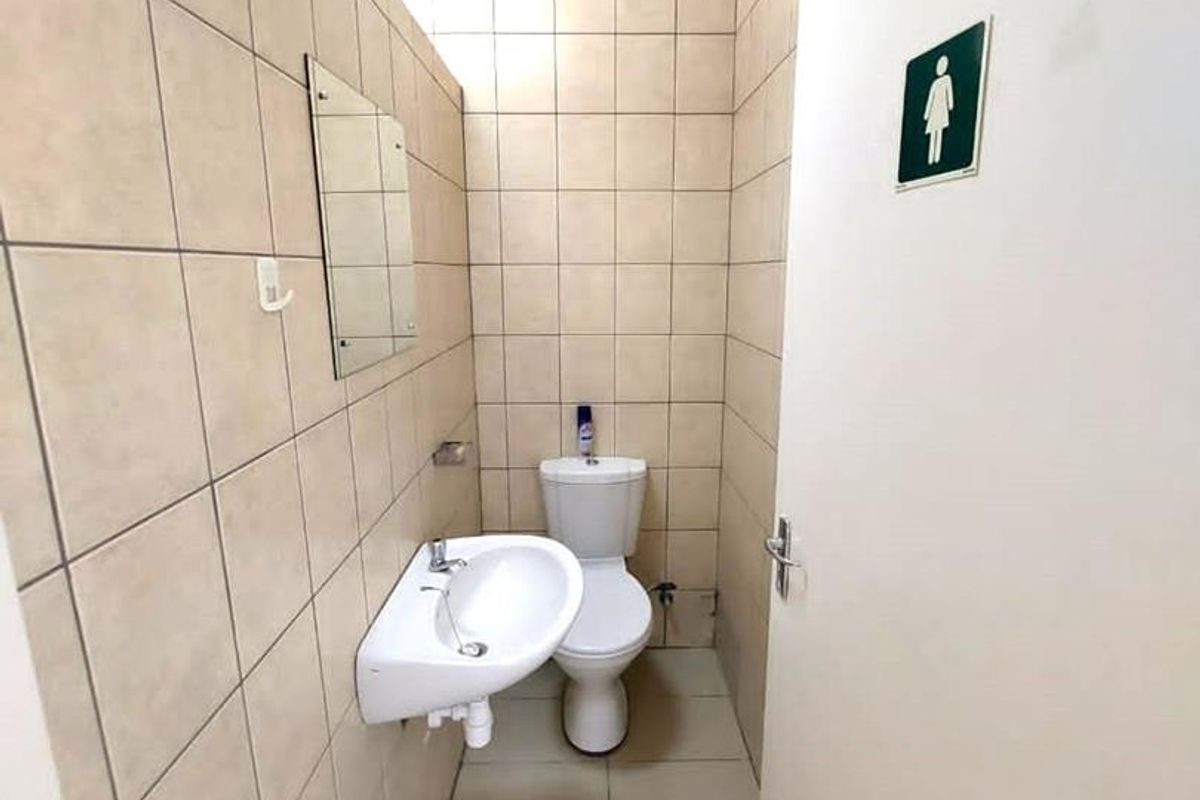 A functional commercial restroom featuring floor-to-ceiling wall tiles, a wall-mounted basin, and a standard toilet suite.