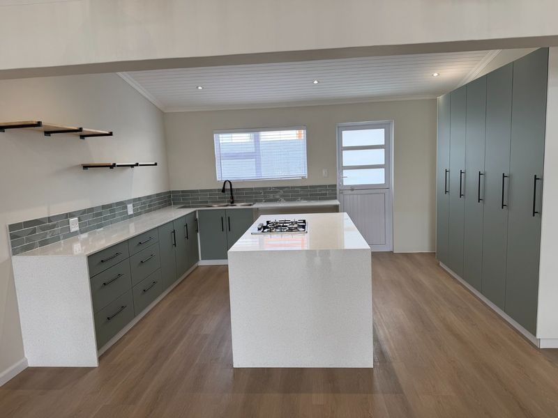 Modern, renovated kitchen featuring sage green cabinetry, white quartz countertops, a central island with a gas hob, and light wood-look flooring.