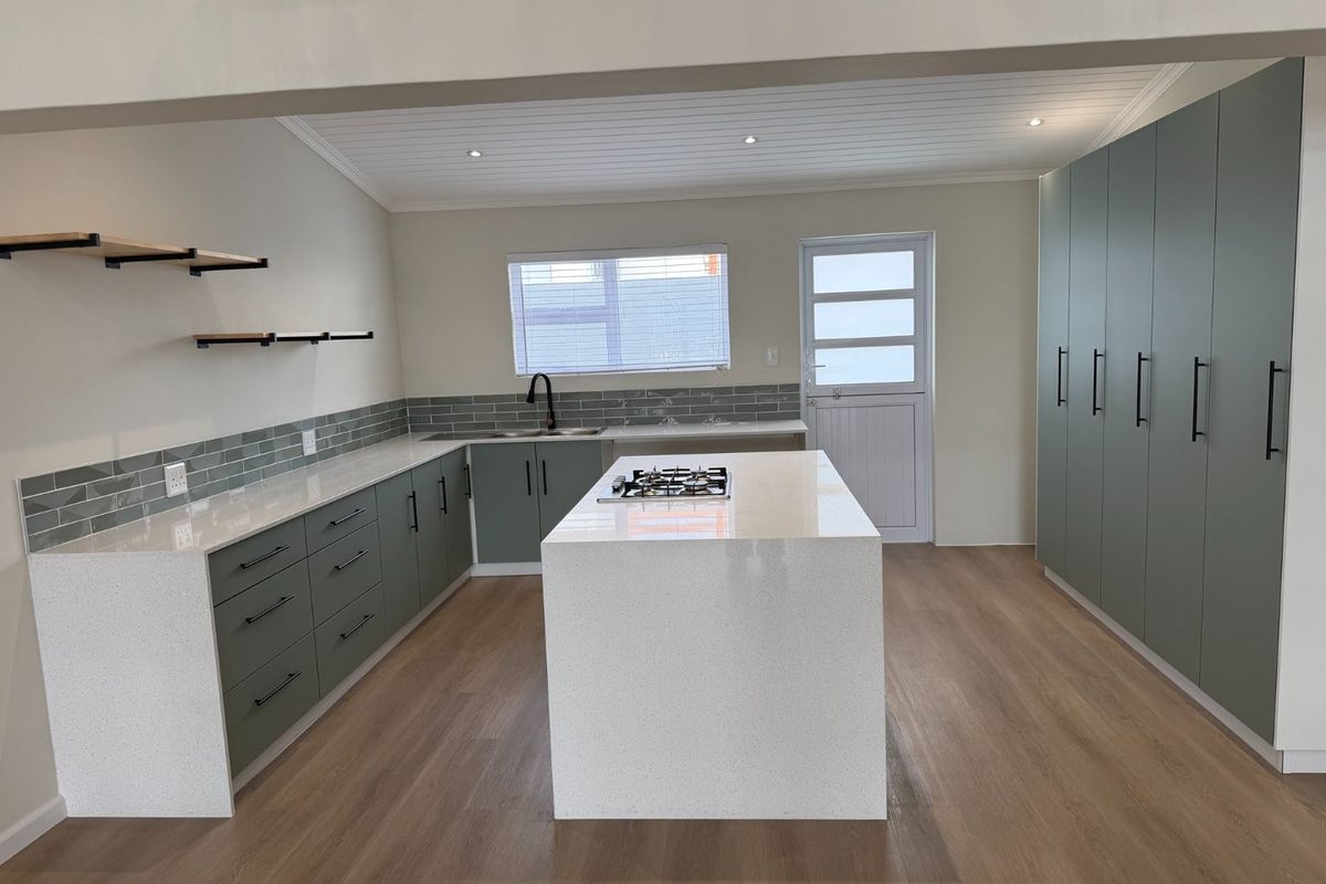 Modern, renovated kitchen featuring sage green cabinetry, white quartz countertops, a central island with a gas hob, and light wood-look flooring.