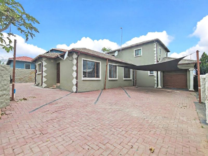 Front exterior view of a multi-level house featuring a large paved driveway, tiled roof, and integrated garage with security features.