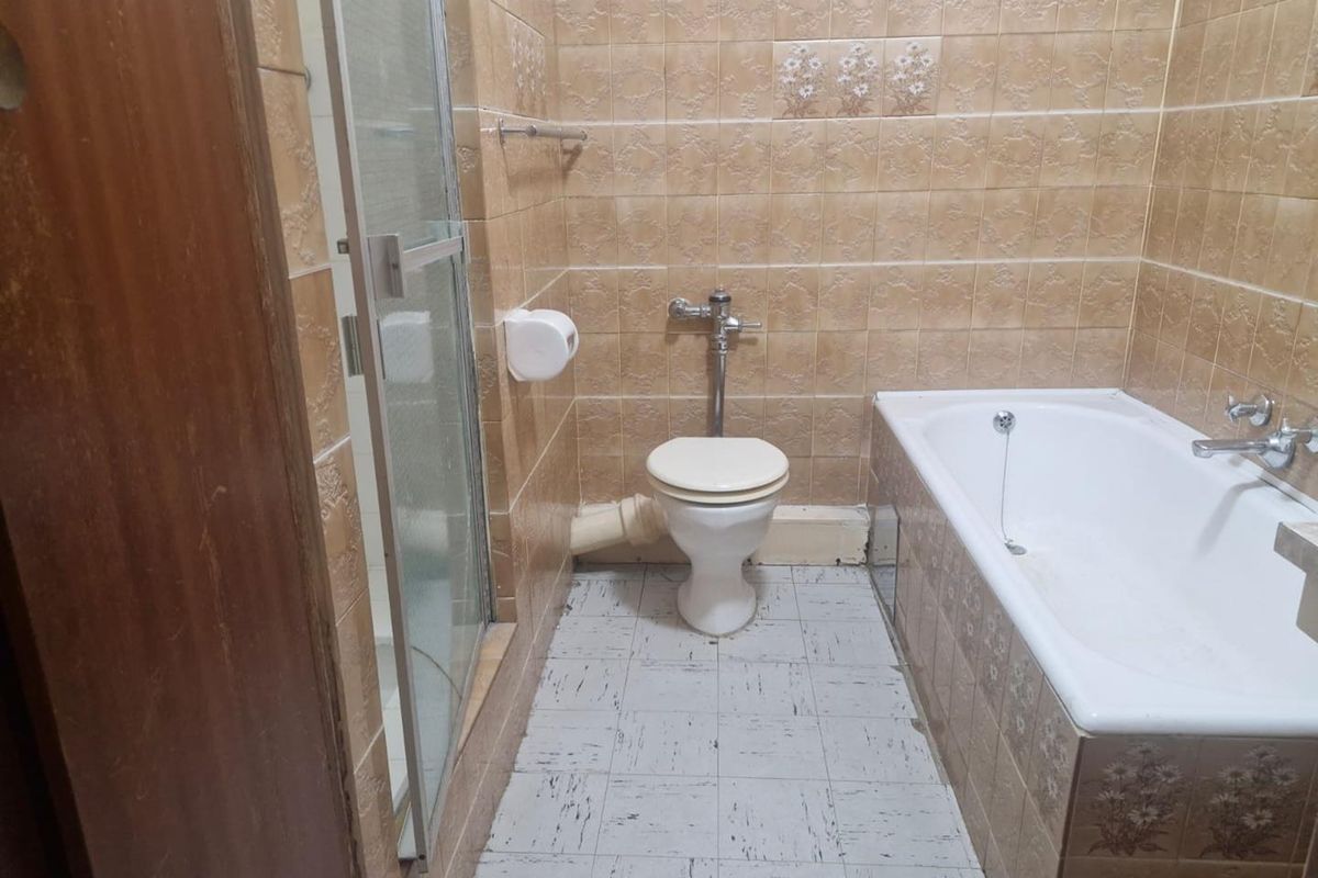A dated bathroom featuring a built-in bathtub, separate shower enclosure, and toilet with exposed plumbing fixtures.
