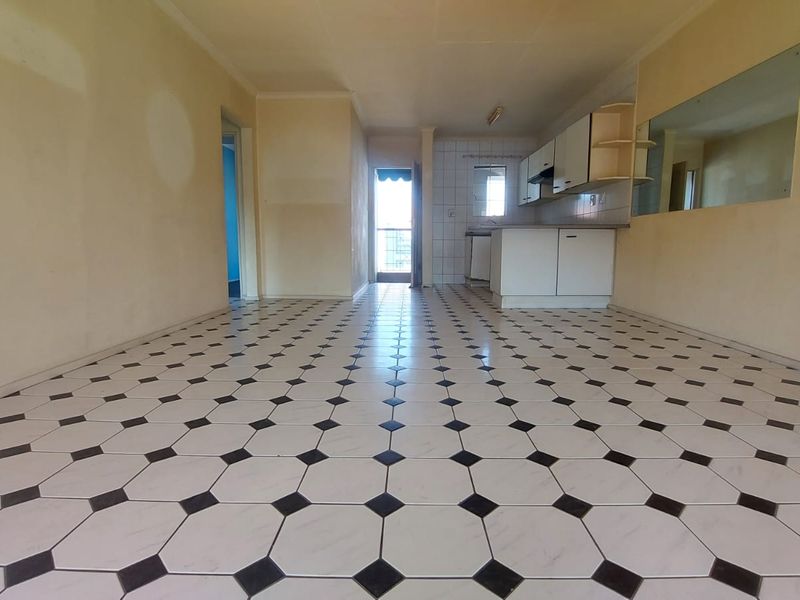An open-plan living and kitchen area featuring distinctive patterned floor tiles, built-in cabinetry, and a wall-mounted mirror, ready for renovation or staging.