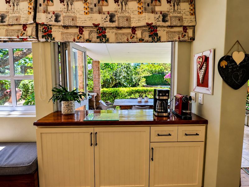 A bright kitchen area featuring built-in cabinetry with a wooden countertop, opening directly onto a covered patio and garden area.
