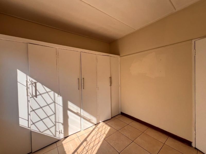 A vacant bedroom featuring built-in cupboards and tiled flooring, requiring minor cosmetic updates to the wall finishes.