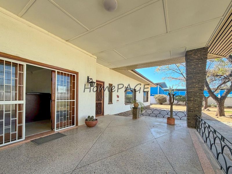 A spacious covered patio featuring terrazzo flooring, a stone-clad support pillar, and wrought iron railings, providing a functional outdoor transition space.