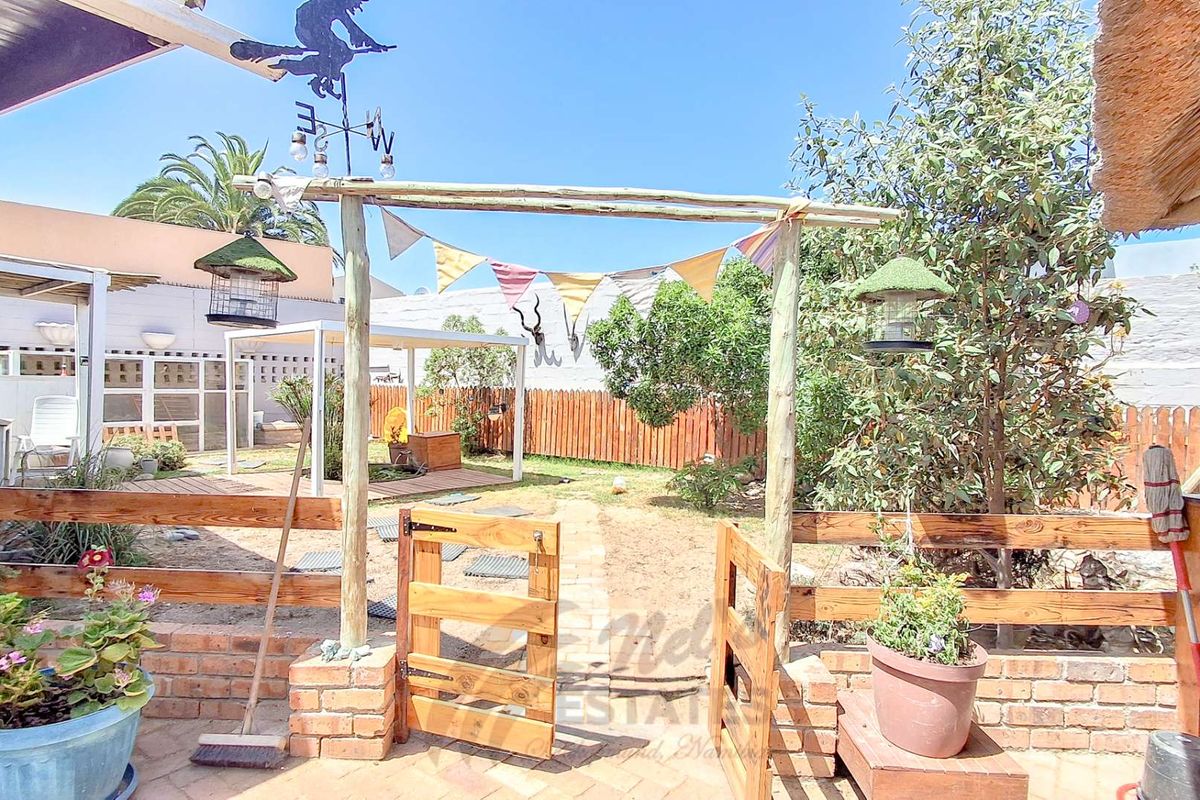 A rear garden area featuring a brick-edged patio, wooden gate, timber fencing, and a small pergola structure in the background.