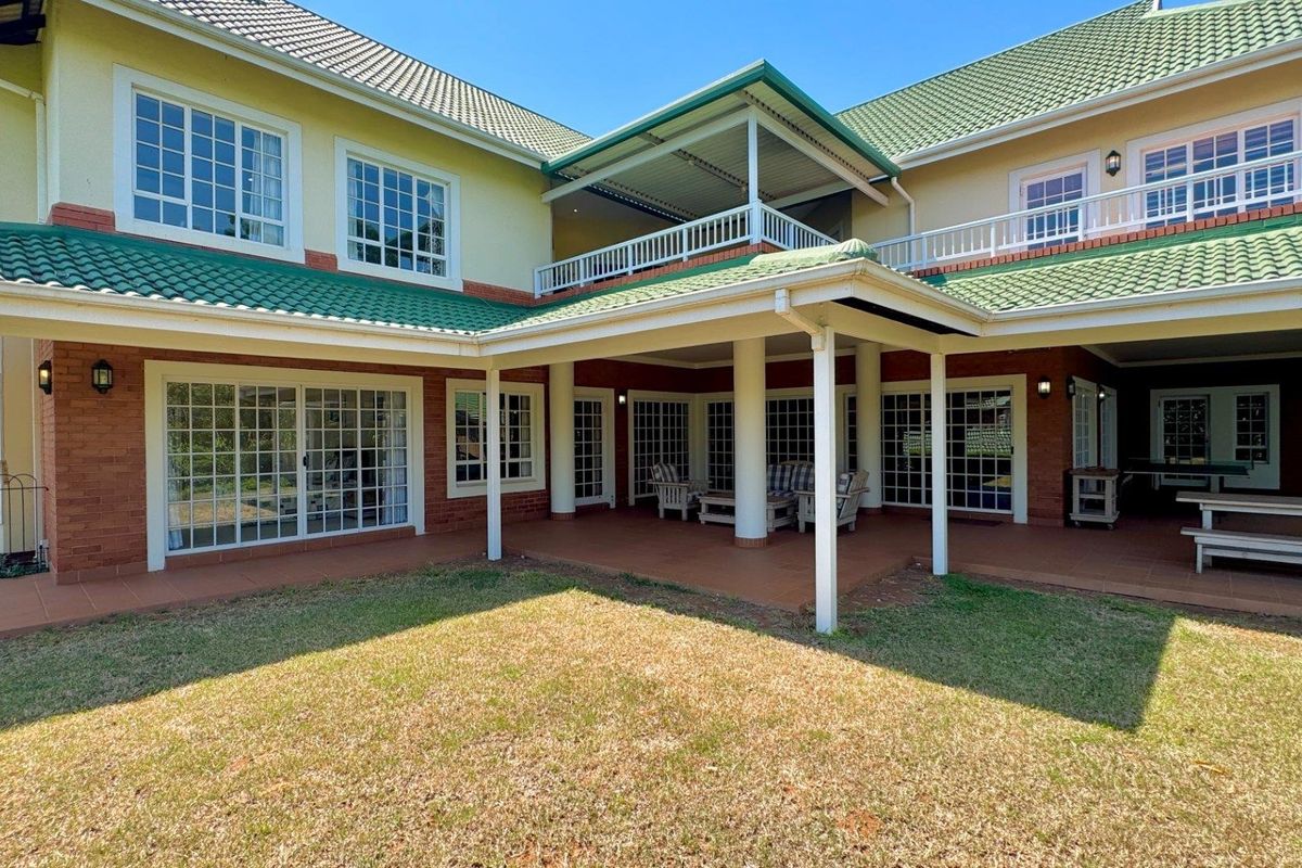 Spacious rear exterior view featuring a large covered patio, upper-level balcony, brick and plaster facade, and green tiled roofing.