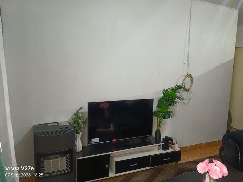 A living room area featuring tiled flooring and visible wall imperfections, requiring minor cosmetic updates and cable management.