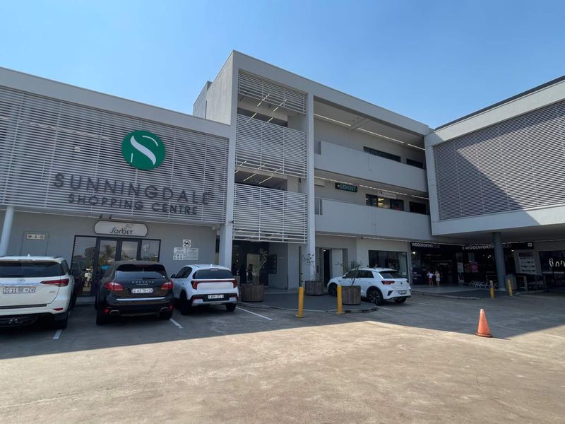 Front elevation of Sunningdale Shopping Centre featuring a modern multi-level retail facade with louvred screening and an open-air concrete parking area.