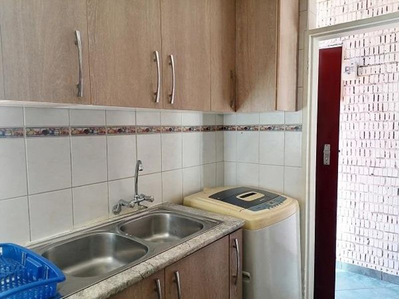 Functional laundry area featuring double stainless steel sink, laminate cabinetry, and tiled backsplash, providing practical utility space.
