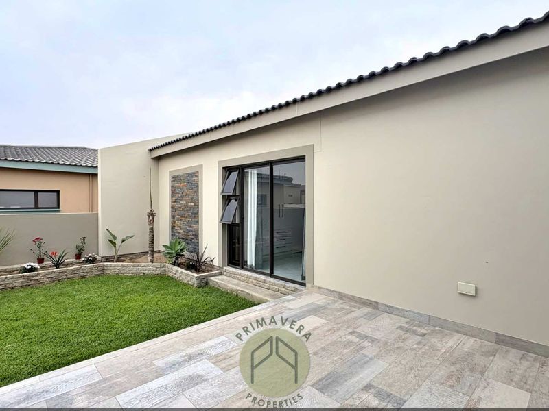 A well-maintained rear exterior featuring a tiled patio, stone-clad feature wall, and a neat garden area with a retaining wall.