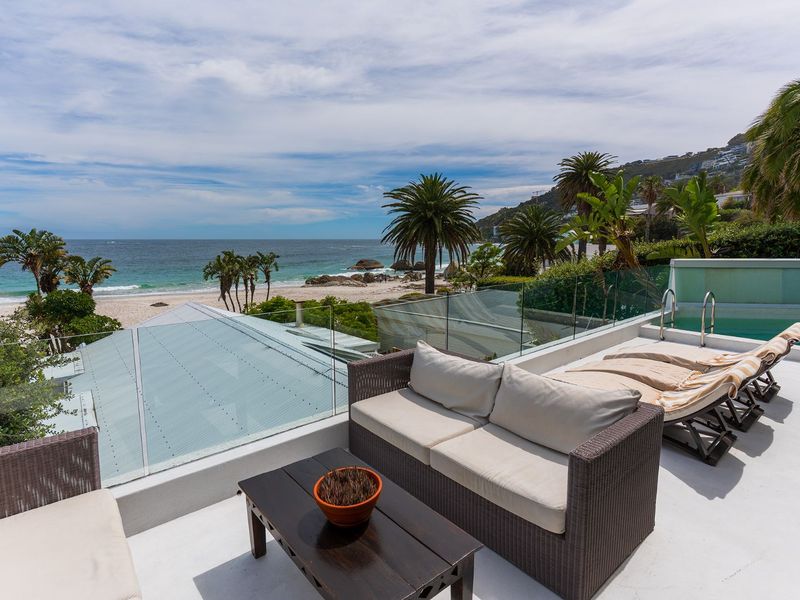 Spacious elevated balcony featuring a glass balustrade and a private swimming pool, offering panoramic ocean and beach views.