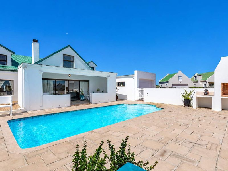 Outdoor entertainment area featuring a swimming pool, paved patio, and a built-in brick braai, set against the rear elevation of the house.