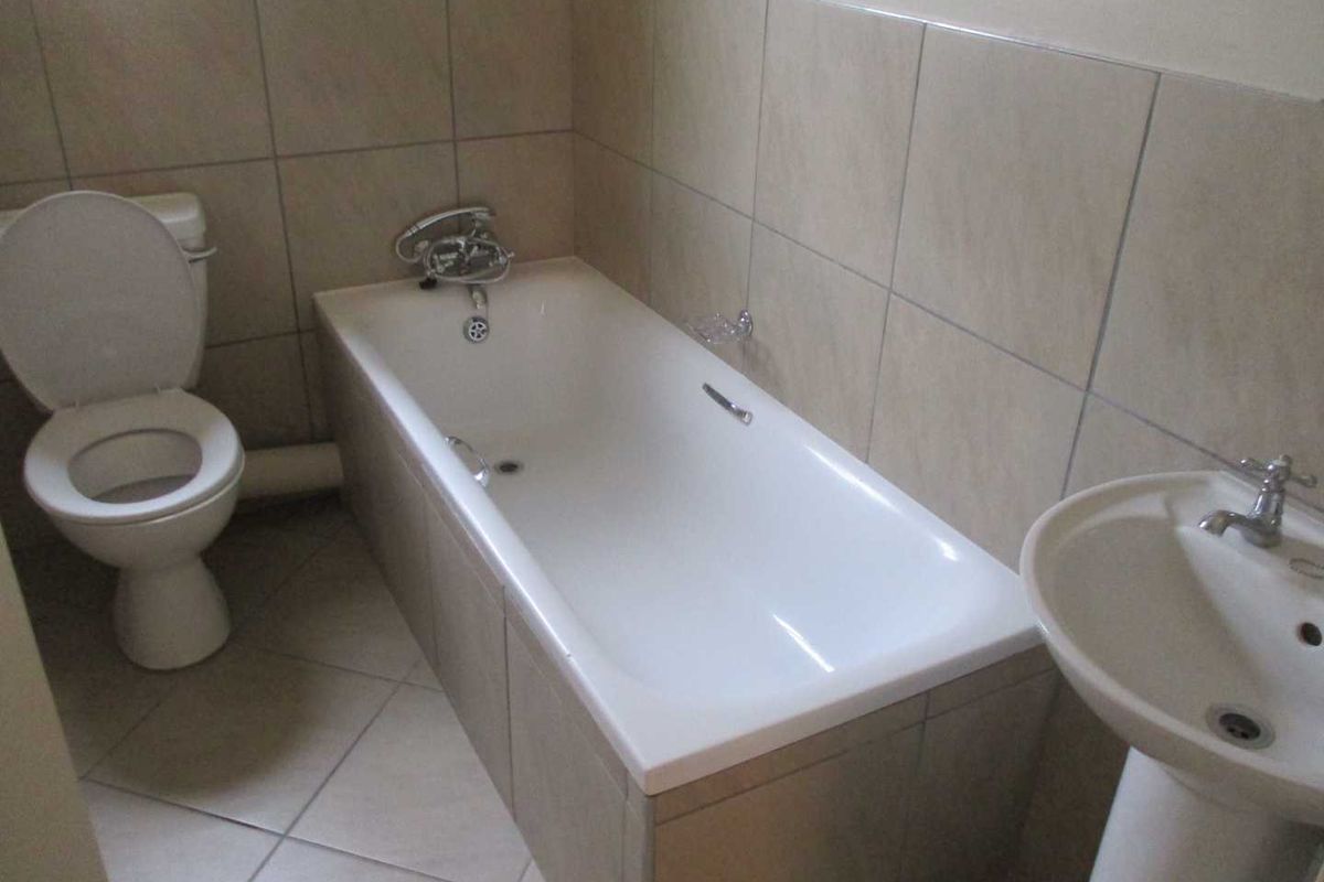 A functional bathroom featuring a standard bathtub, pedestal basin, and toilet with neutral ceramic wall and floor tiling.