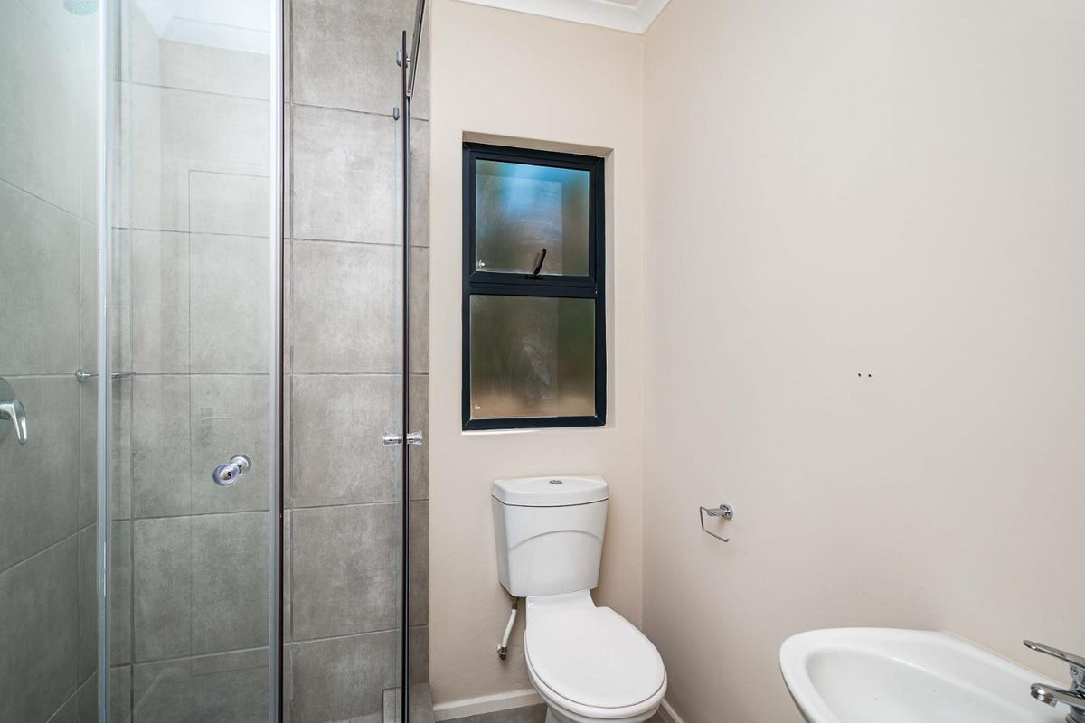 A modern bathroom featuring a glass-enclosed shower with grey tiled walls, a white toilet, and a pedestal basin.