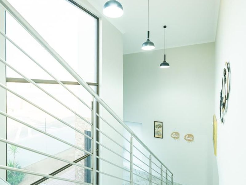 A bright and modern staircase area featuring sleek stainless steel balustrades, large floor-to-ceiling windows, and contemporary pendant lighting.