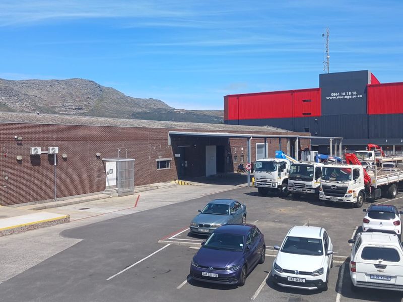 Industrial property exterior featuring a brick facade, loading bay with roller shutter door, and an expansive asphalt parking area.