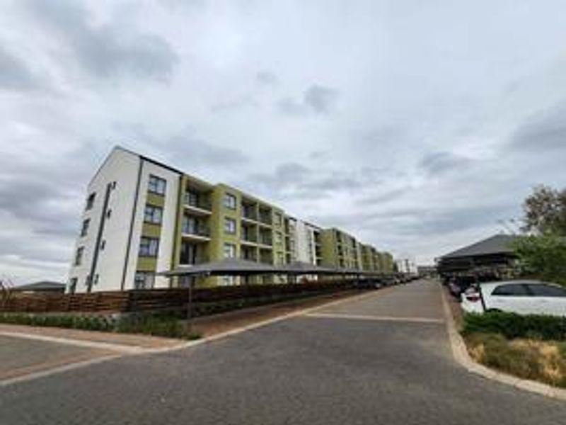 Exterior view of a multi-story apartment complex featuring covered parking bays and paved driveway access.