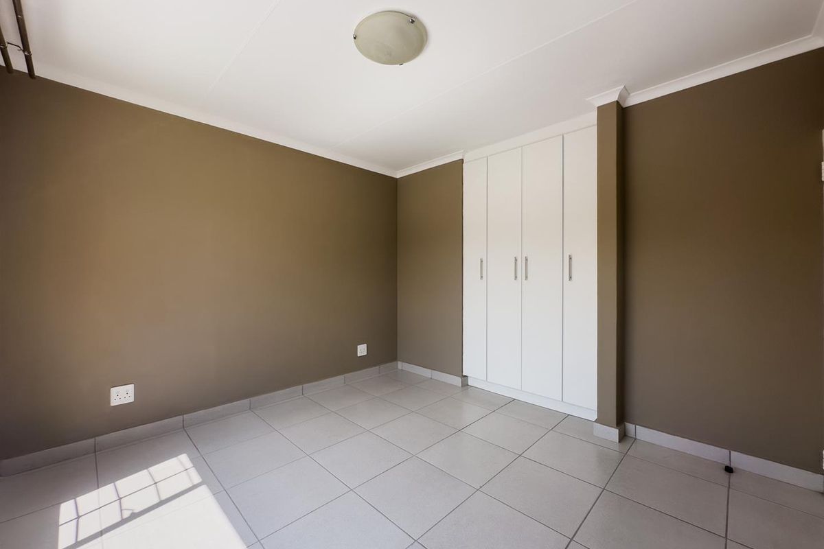 A clean, empty bedroom featuring neutral brown walls, white built-in cupboards, and light-colored floor tiles.