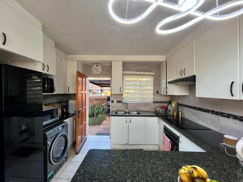 Functional kitchen featuring granite countertops, built-in cabinetry, electric hob, oven, and direct access to the rear exterior area.