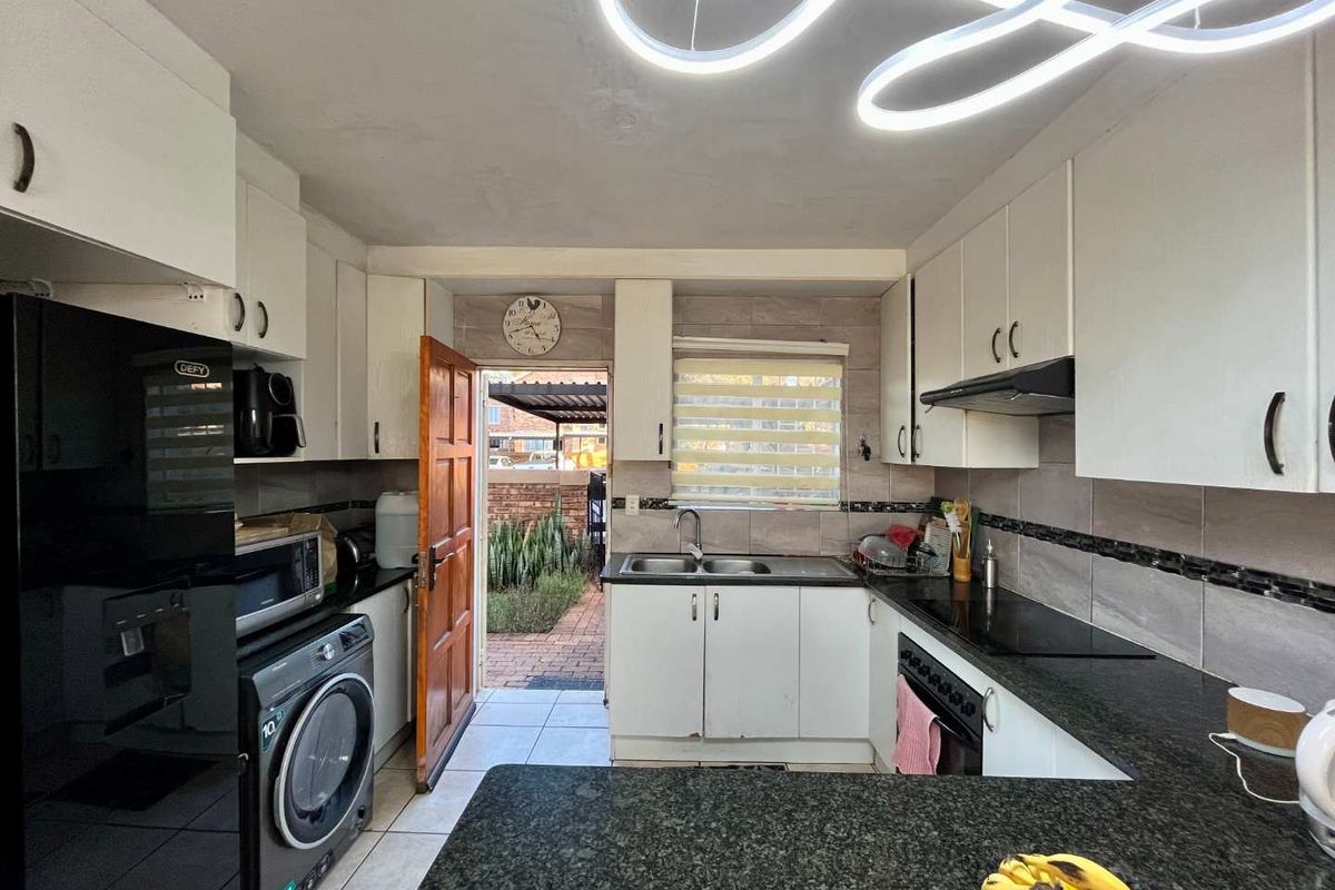Functional kitchen featuring granite countertops, built-in cabinetry, electric hob, oven, and direct access to the rear exterior area.